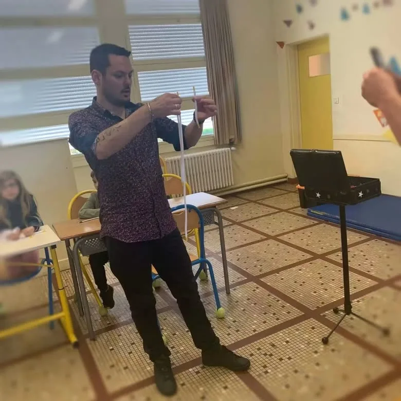 Jérôme présente un tour de corde devant une classe, sa malle ouverte derrière lui