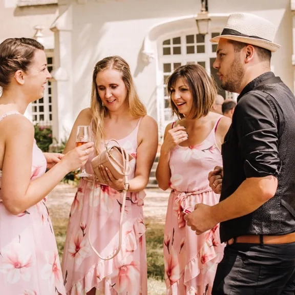 Jérôme présente un tour à un groupe d'invitées en robes fleuries, devant la façade d'un château