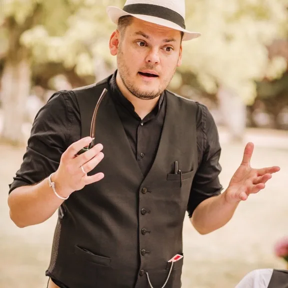 Jérôme en gilet noir et chapeau, mains ouvertes en pleine narration sous une lumière dorée en contre-jour