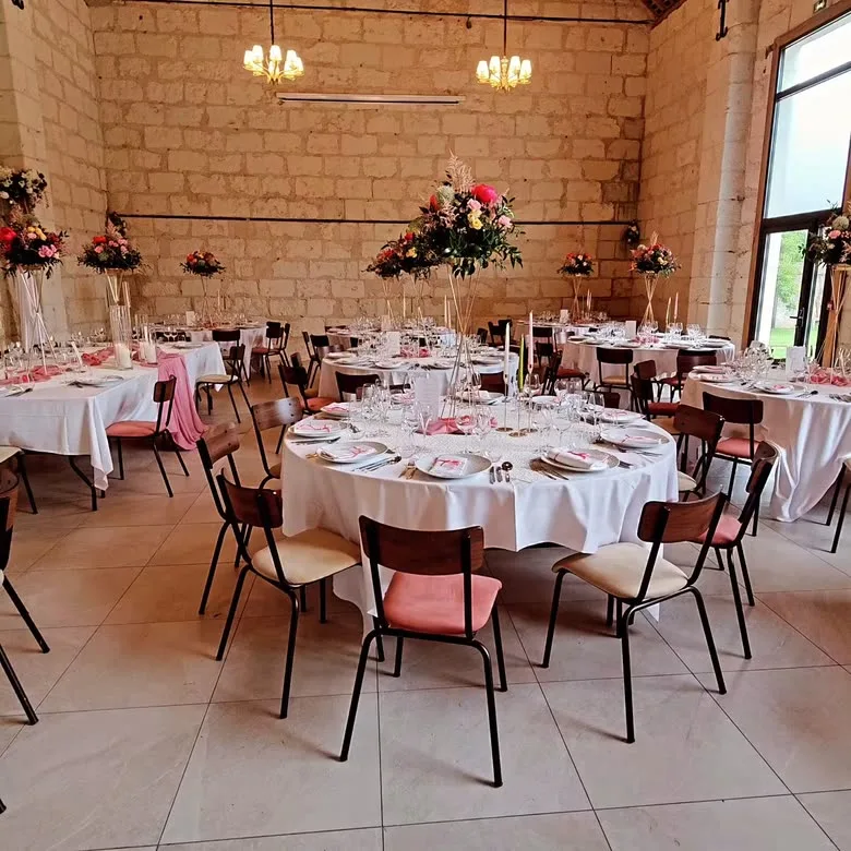 Salle voûtée en pierre dressée pour un repas, tables rondes et hautes compositions florales